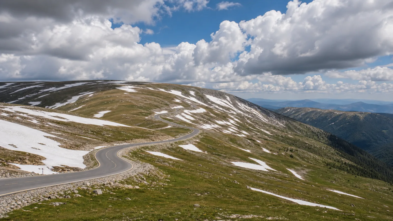 Transalpina la început de vară, cu petice de zăpadă topindu-se pe pantele alpine de lângă asfalt