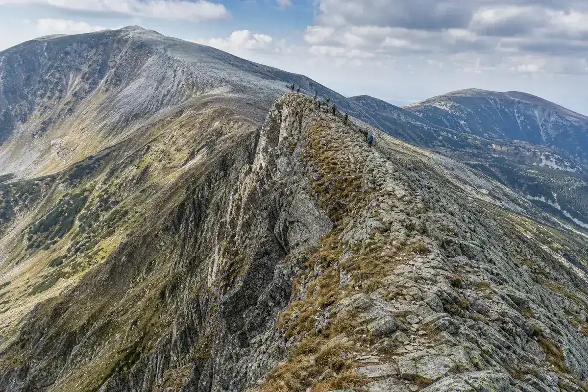 Creastă alpină stâncoasă în Munții Parâng, cu drumeți mici pe linia crestei și abisuri de o parte și de alta