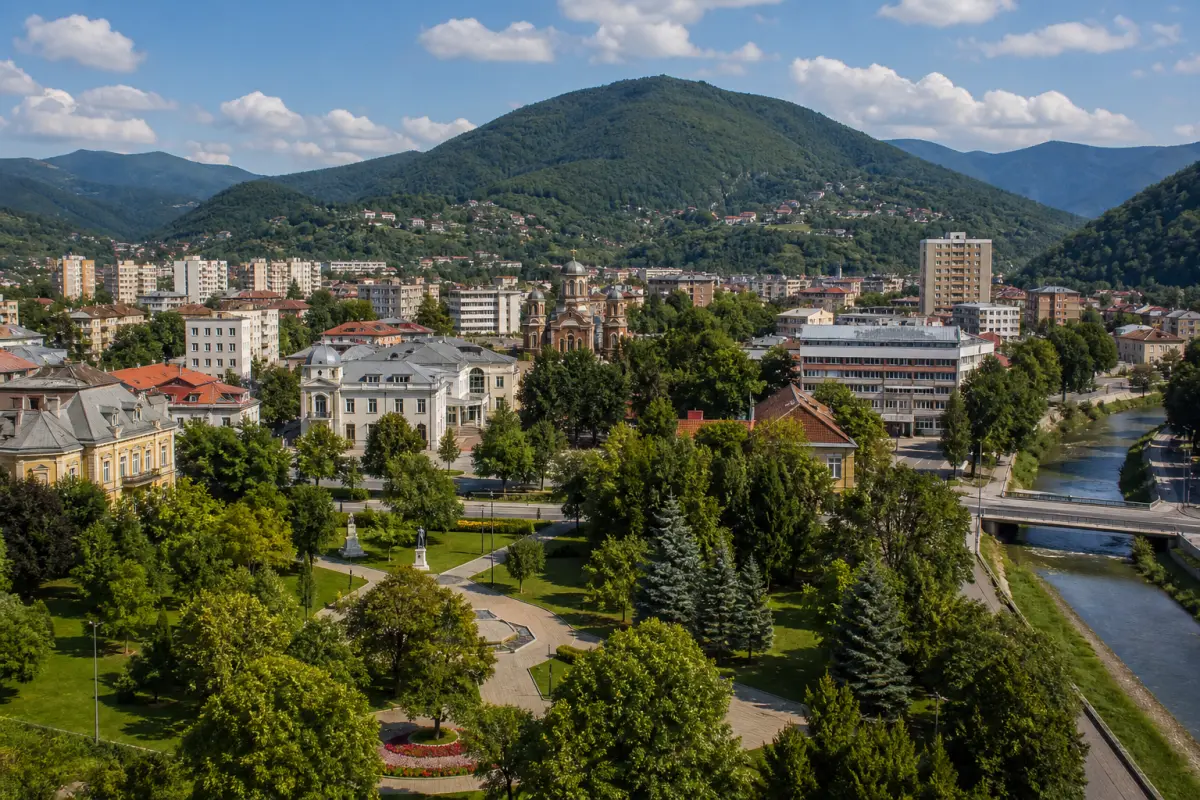 Oraș mic românesc într-o vale verde de râu, înconjurat de dealuri, cu parc central